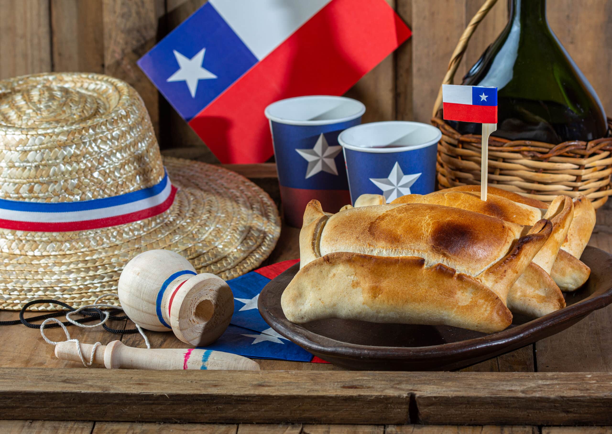 Chilean independence day concept. fiestas patrias. Tipical baked empanadas de pino, wine or chicha, hat and play emboque. Dish and drink on 18 September party, wooden background.